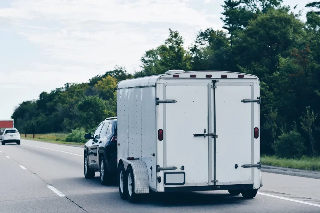 Black SUV towing a white enclosed trailer on a highway, illustrating safe towing practices.