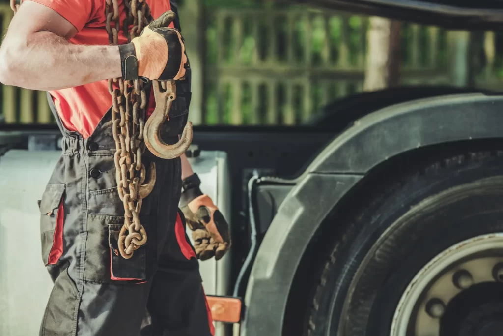 Close-up of a towing service worker holding heavy-duty load support chains and a hook, prepared for complex towing tasks.