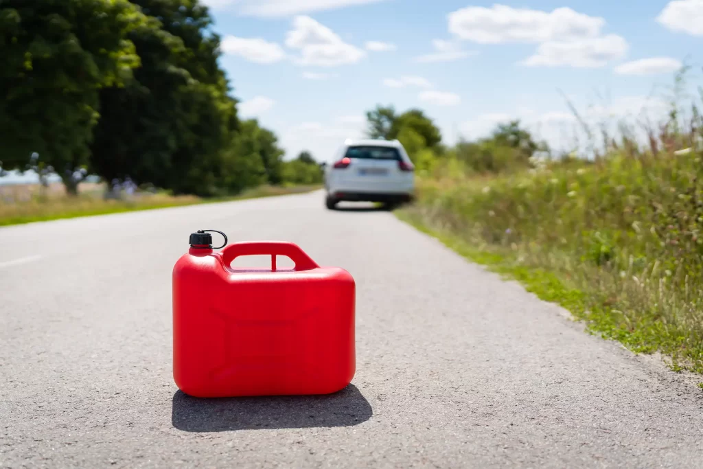 An empty red fuel can on the roadside with a car in the background, highlighting the need for emergency fuel delivery services.