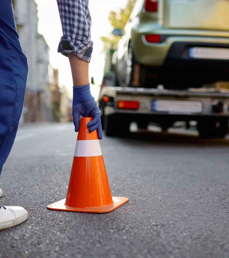 a driver placing a cone on the road with a tow truck in the background