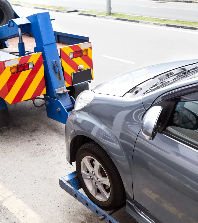 A tow truck carrying and directing a car using a crane at the back